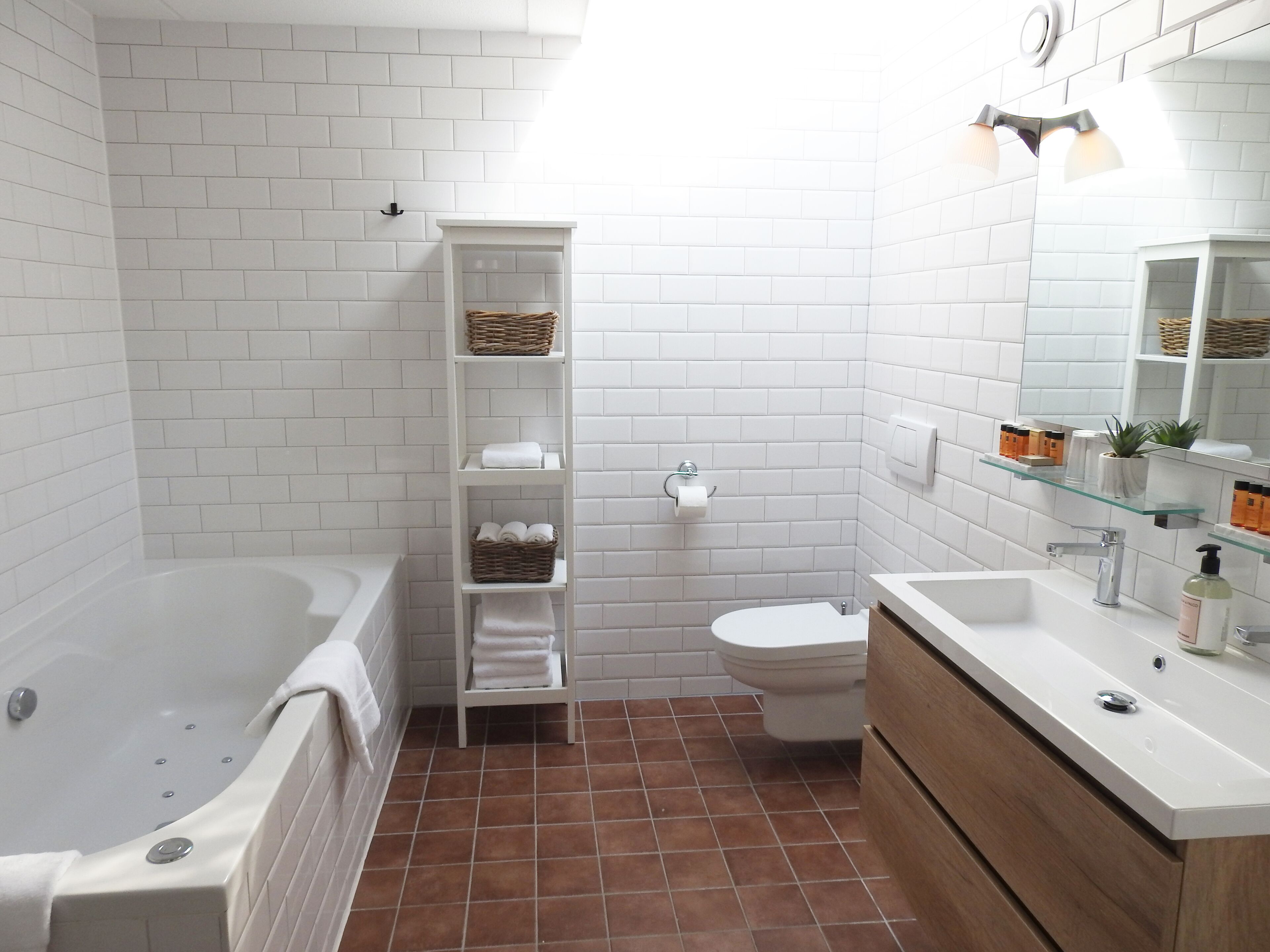 A bathroom with a bathtub, toilet, and vanity with a mirror. There are shelves with towels and toiletries.