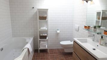 A bathroom with a bathtub, toilet, and vanity with a mirror. There are shelves with towels and toiletries.