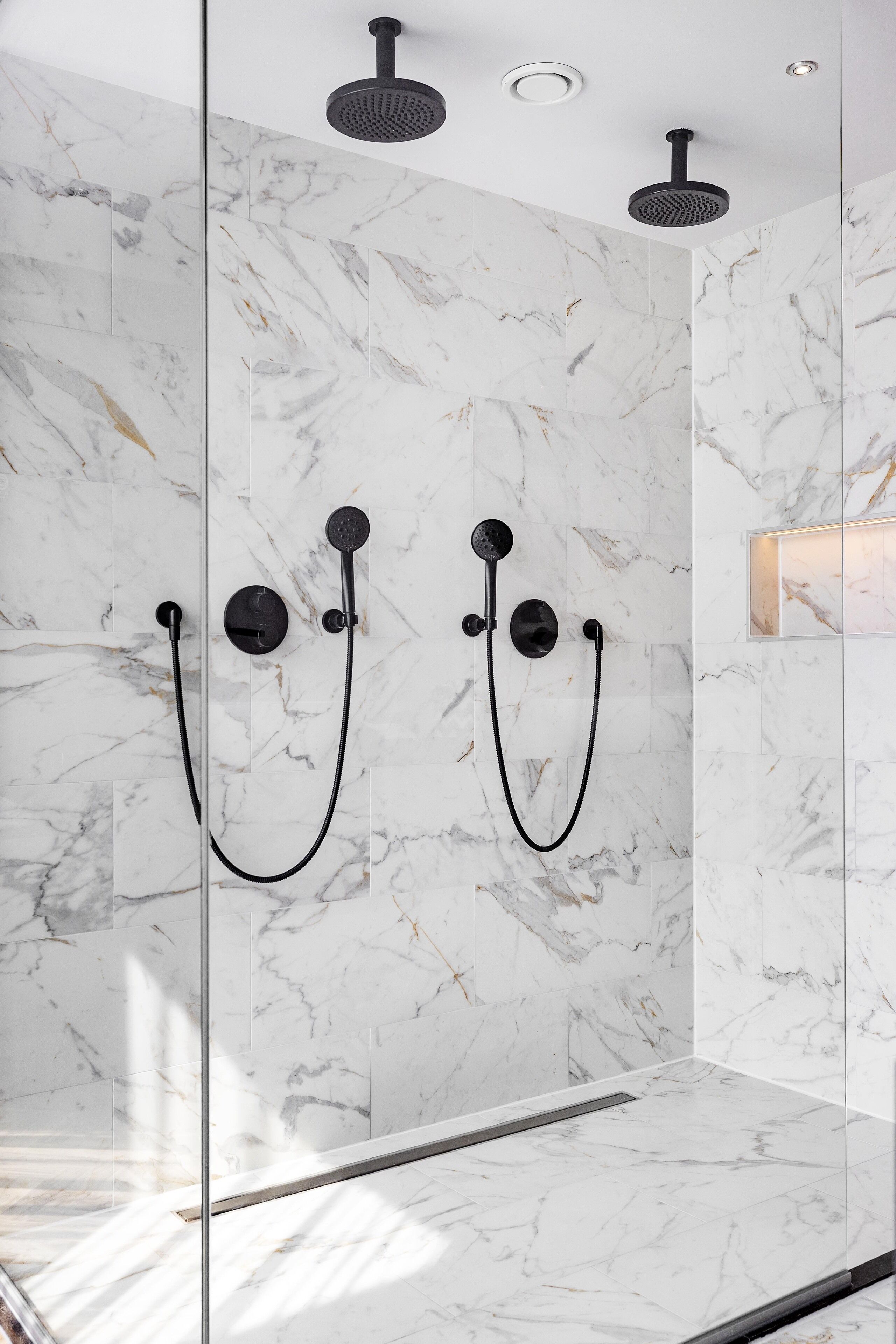 A modern shower with a glass enclosure, marble walls, and a ceiling-mounted showerhead.