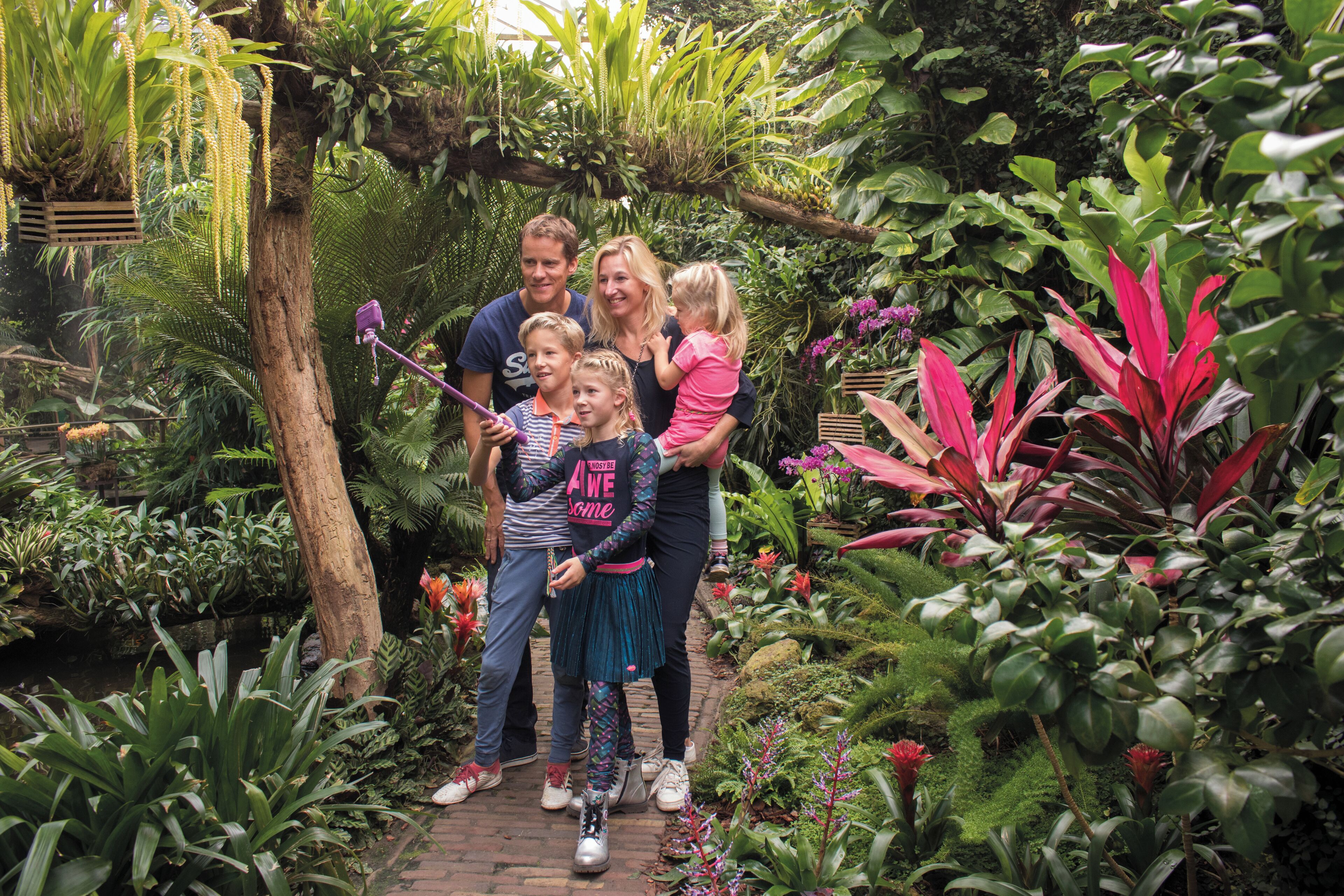 A family in a lush garden with dense foliage and a variety of plants.