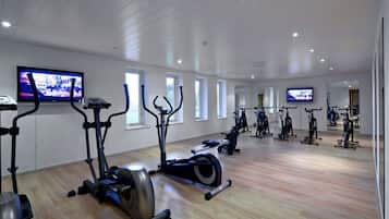 Ein geräumiges Fitnessstudio mit verschiedenen Cardiogeräten, großen Fenstern und einem Flachbildfernseher an der Wand.