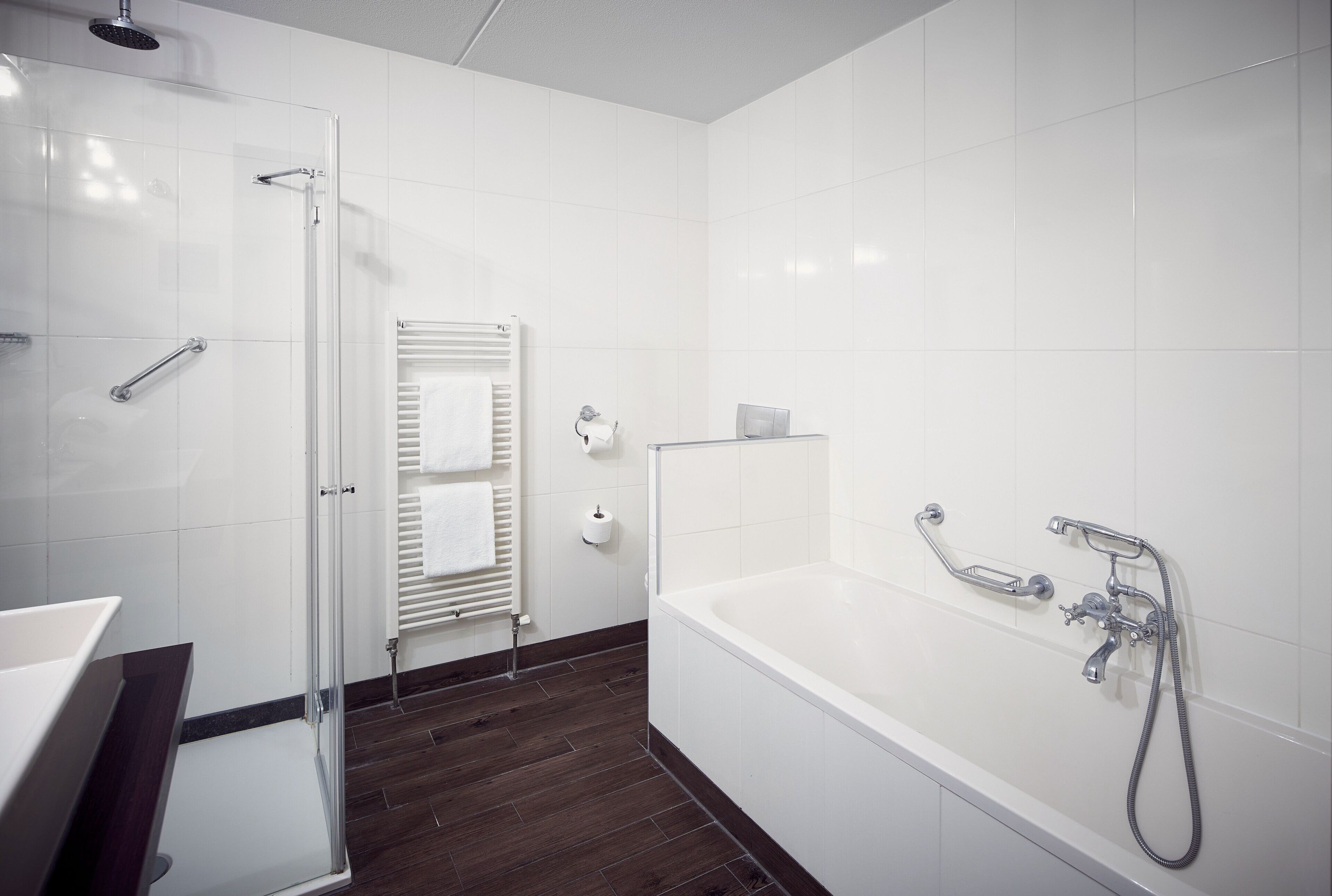 A modern bathroom with a glass shower enclosure, a white bathtub with a handheld showerhead, and a towel rack with towels.