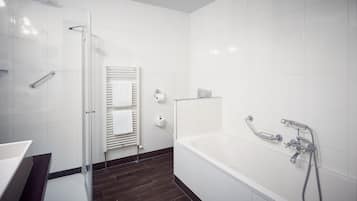 A modern bathroom with a glass shower enclosure, a white bathtub with a handheld showerhead, and a towel rack with towels.
