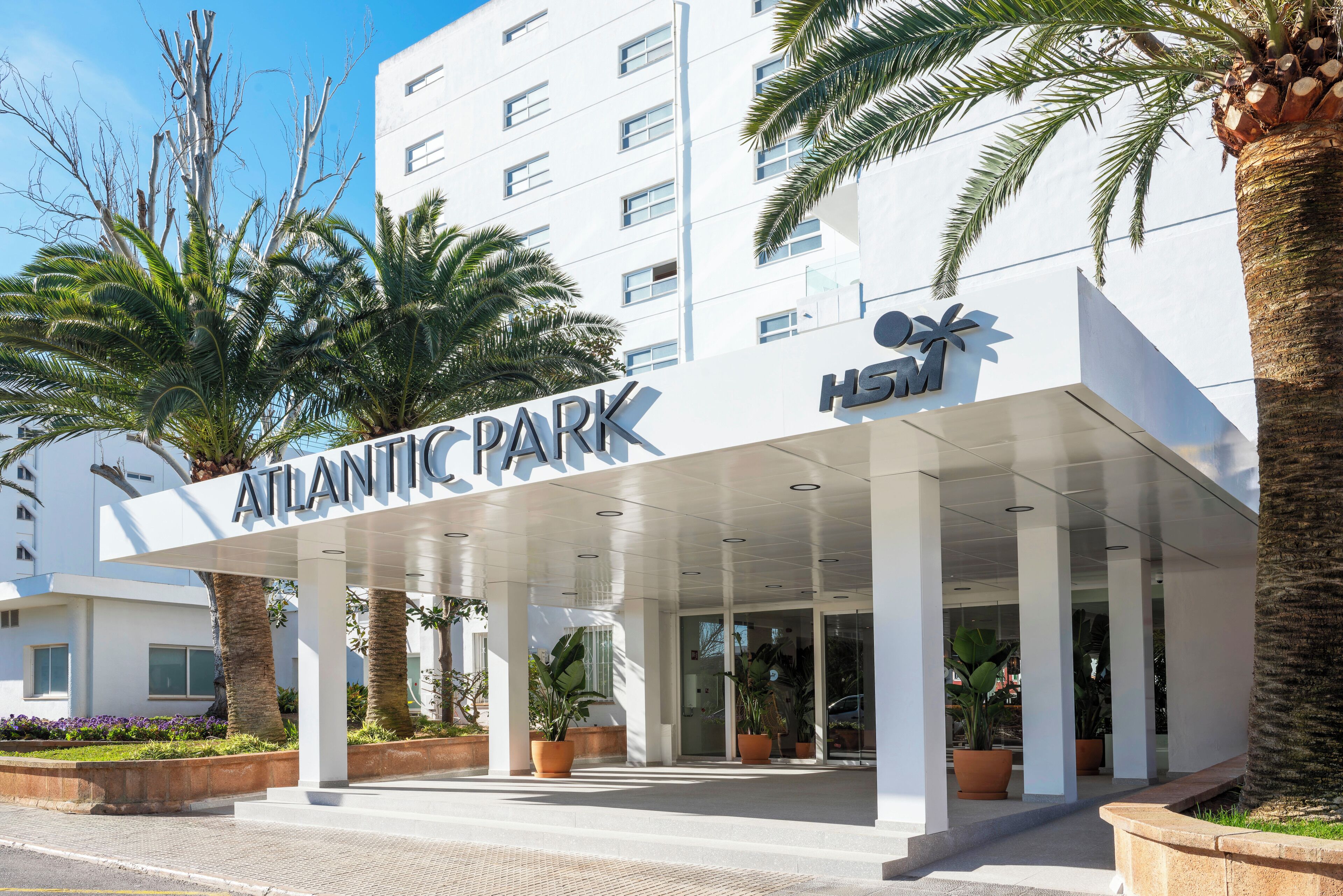The exterior of the Atlantic Park hotel with a covered entrance, palm trees, and a clear sky.