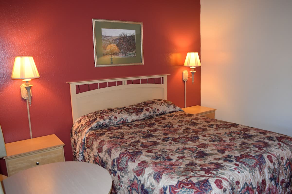 A bedroom with a floral bedspread, two bedside lamps, a nightstand, and a round table.