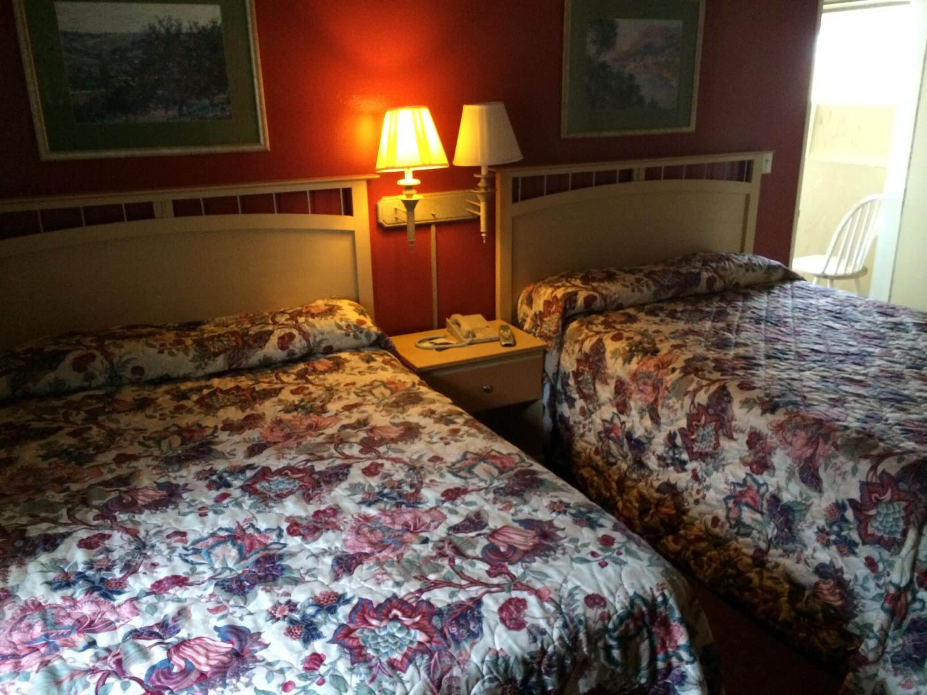 A hotel room with two beds, each with floral bedding, a bedside table with a lamp, and a phone.