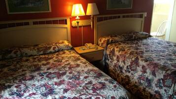 A hotel room with two beds, each with floral bedding, a bedside table with a lamp, and a phone.