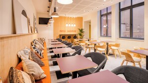 En moderne café med flere borde og stole, en trævæg med skiltet 'Hello sunshine' og store vinduer.