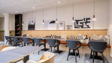 Un espace de restauration moderne avec des tables et des chaises, un banc en bois et des luminaires suspendus.