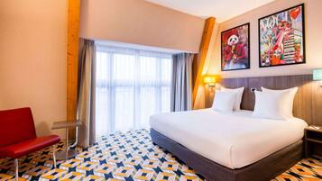 A hotel room with a large bed, a red chair, and two wall art pieces.