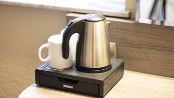 Una cafetera y una taza sobre un soporte negro en una habitación de hotel.