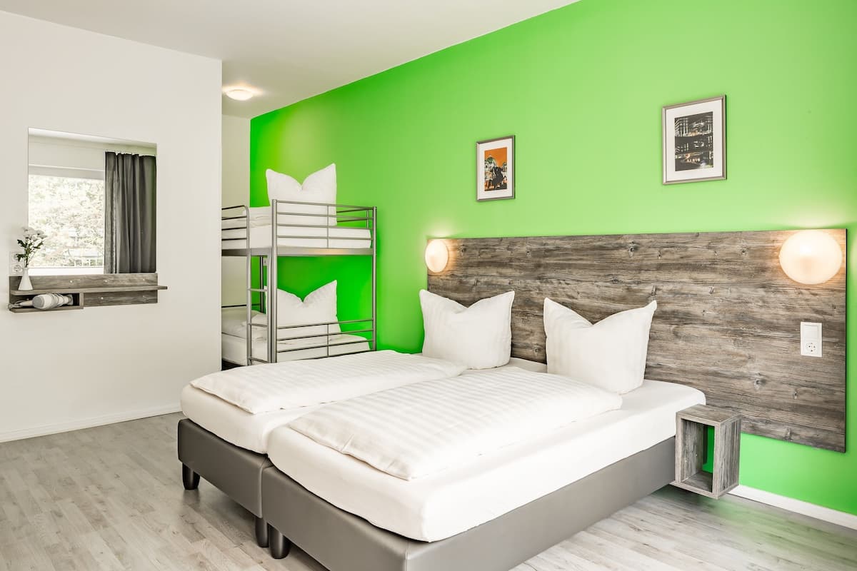 A modern bedroom with a bunk bed, a large bed, and a green accent wall.