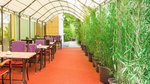 Un área de estar al aire libre cubierta con mesas y sillas, rodeada de plantas en macetas.