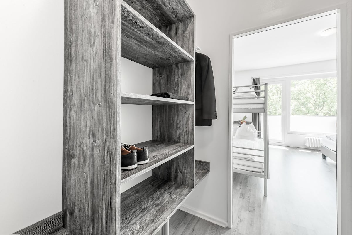 A modern room with a wooden shelving unit, a bunk bed, and a view of greenery outside.