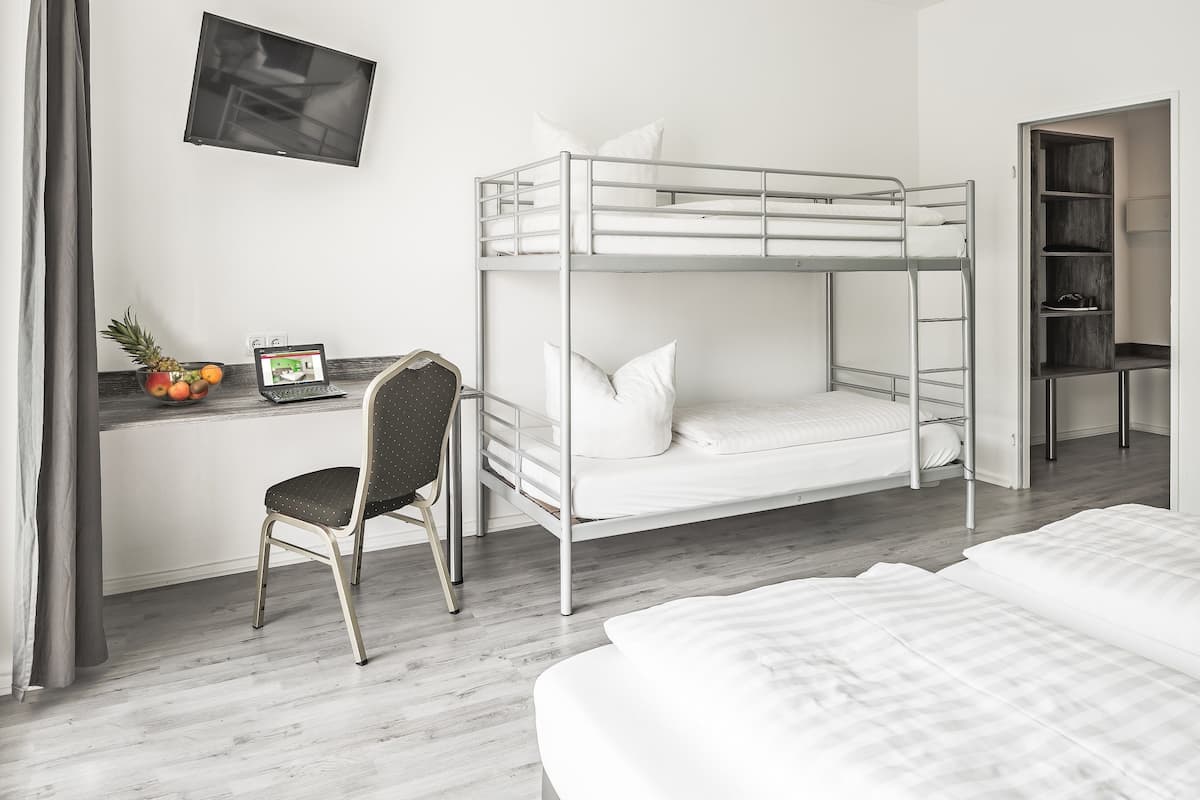 A bunk bed room with a desk, chair, and a TV mounted on the wall.