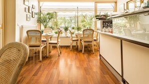 Un comedor con sillas de mimbre, piso de madera, ventanas amplias y plantas en macetas.