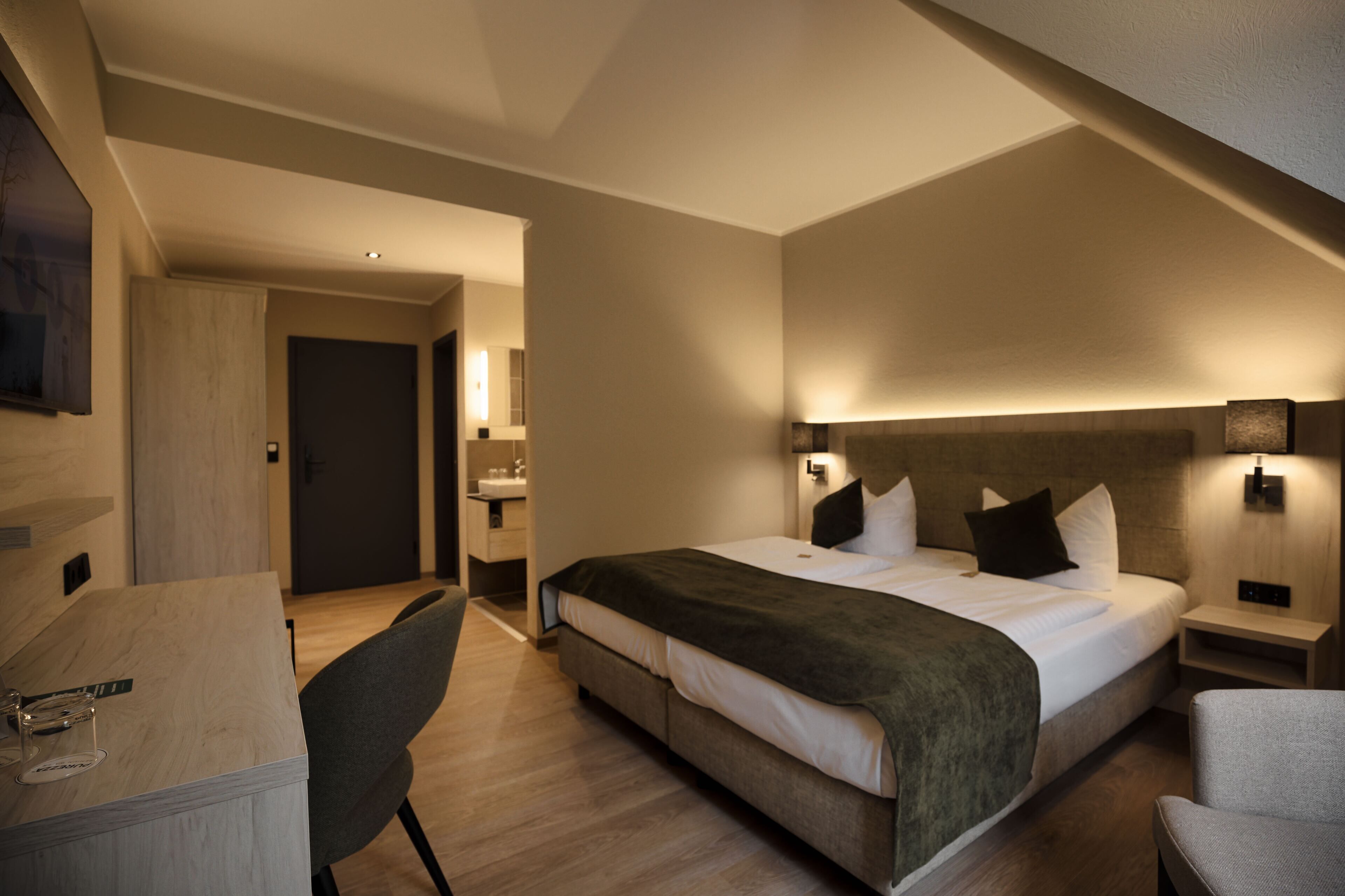 A hotel room with a bed, bedside tables, a desk, and a chair.