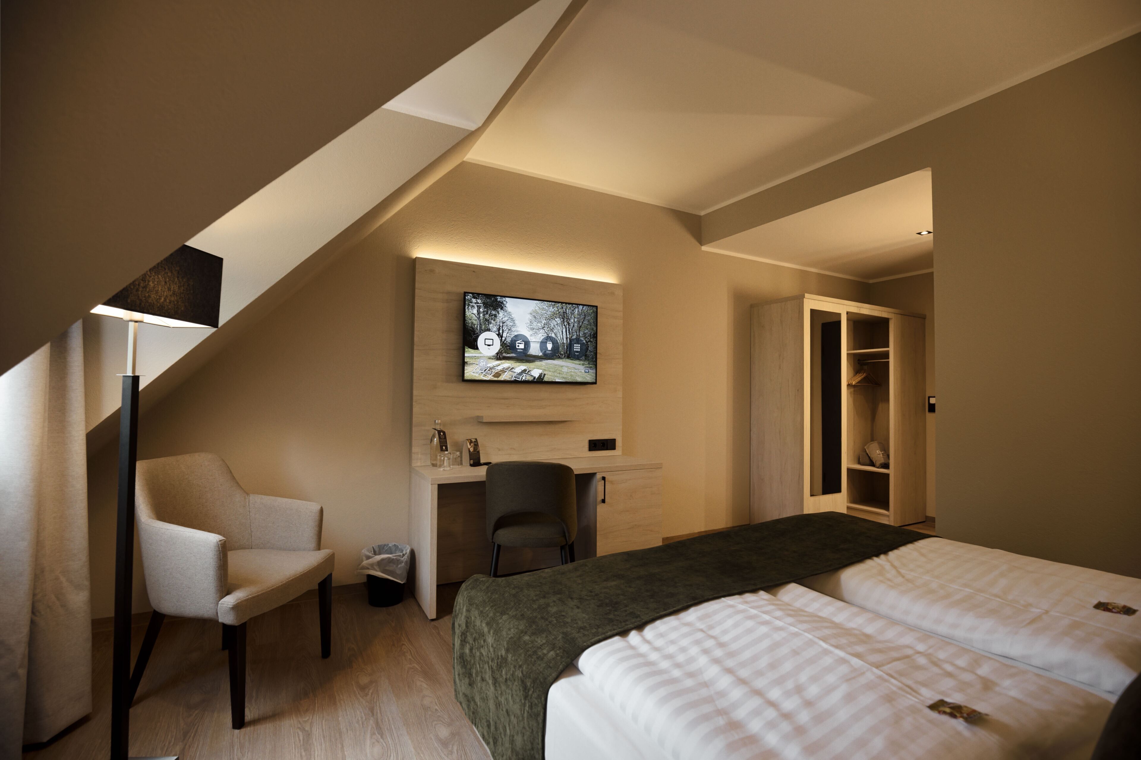 A hotel room with a bed, desk, chair, TV, and wardrobe.