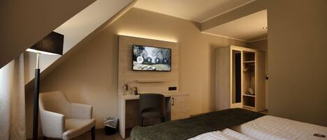 A hotel room with a bed, desk, chair, TV, and wardrobe.
