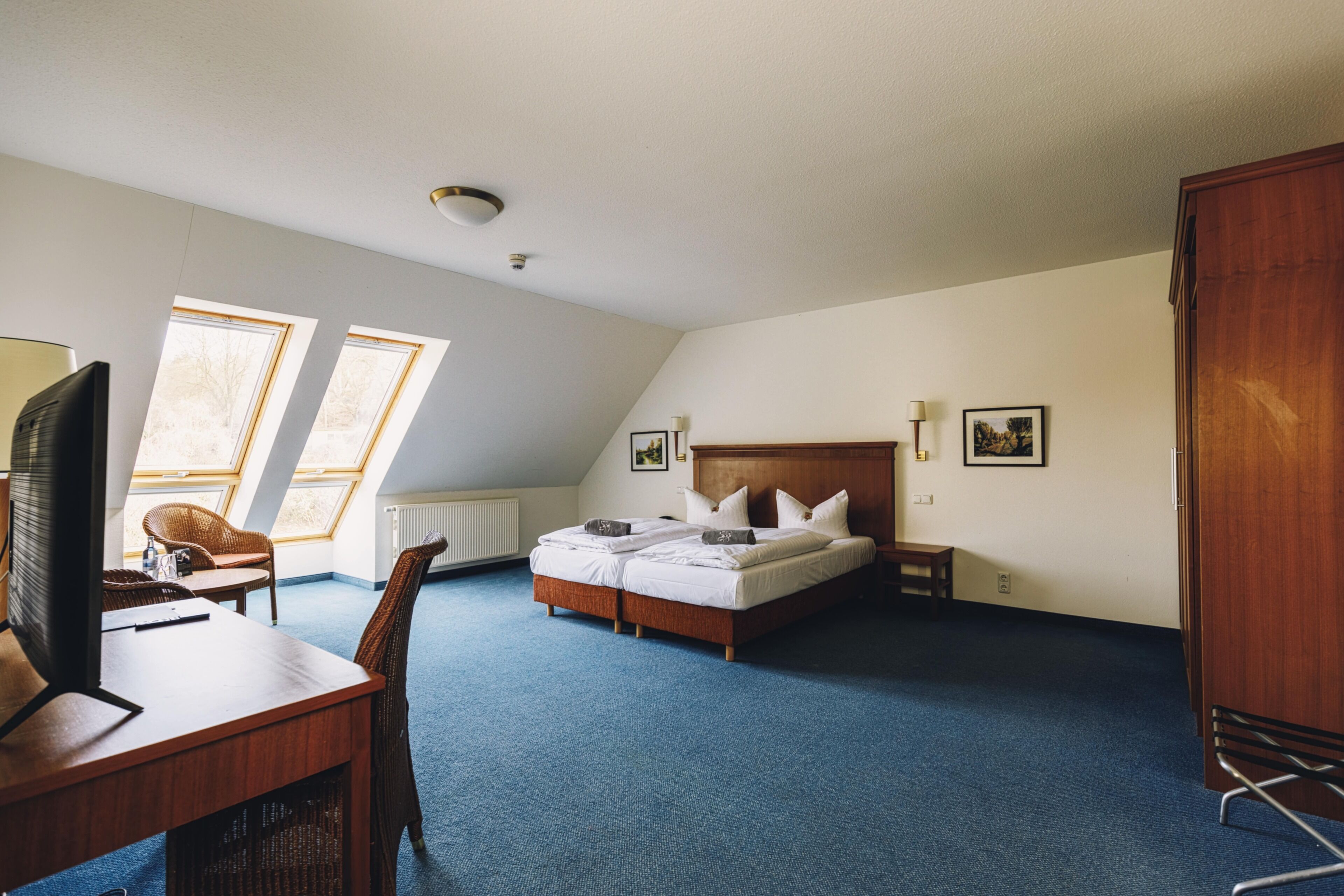 A hotel room with a bed, a desk with a computer, a chair, and two windows.