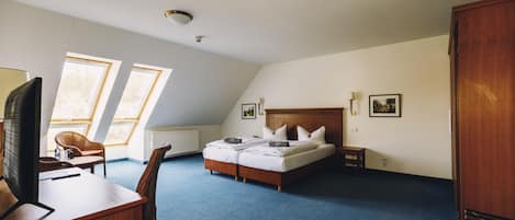 A hotel room with a bed, a desk with a computer, a chair, and two windows.