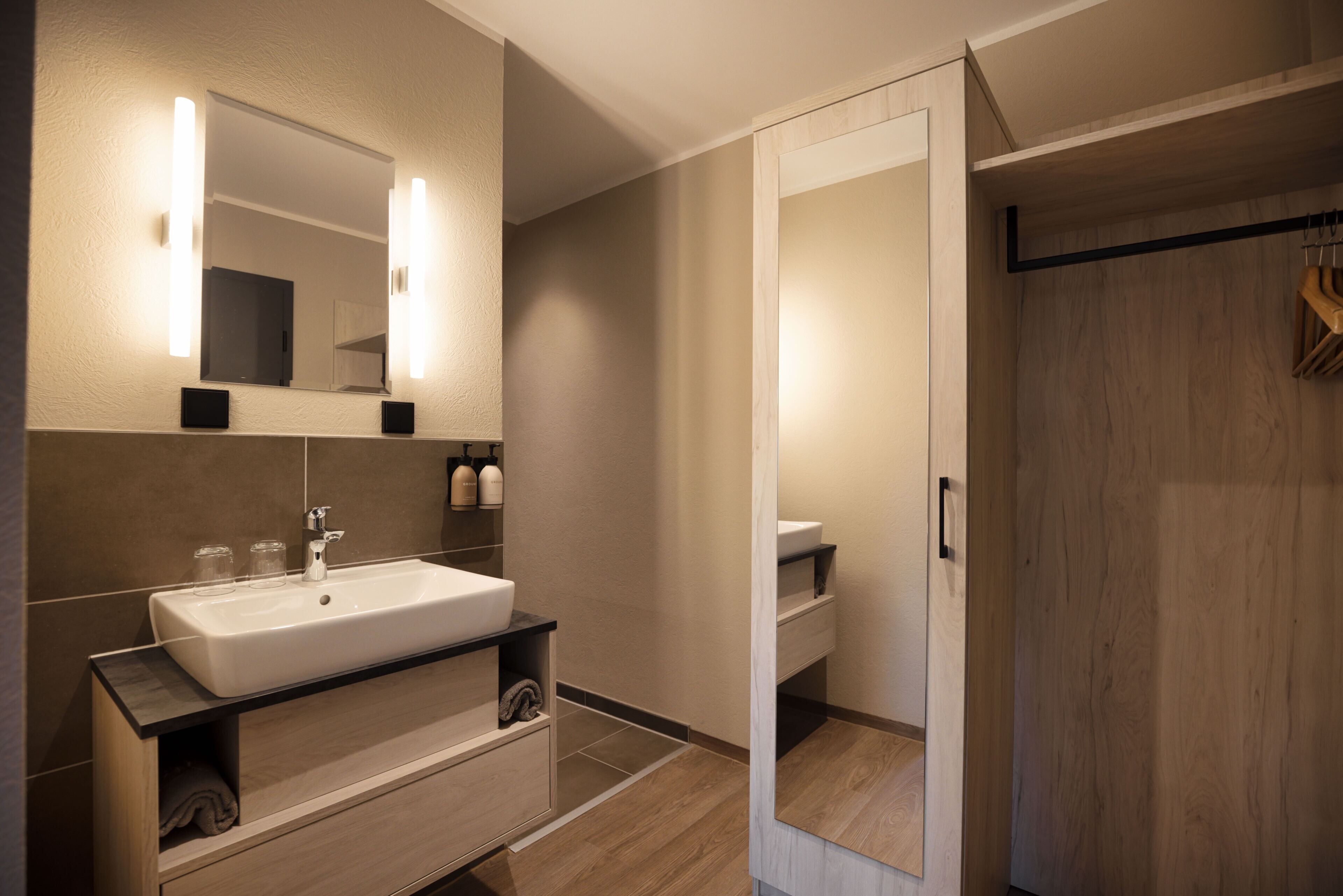 A modern bathroom with a large mirror, a sink, and a wooden vanity.