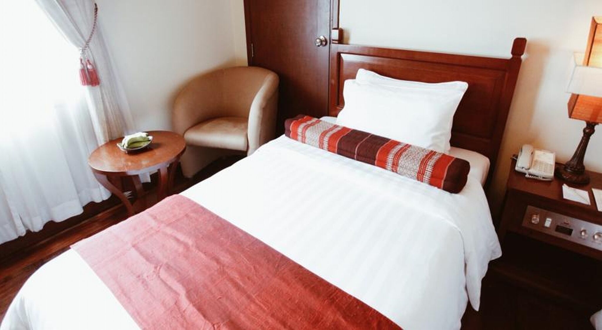 Hotellihuone, jossa on sänky, tuoli, pieni pöytä, yöpöytä ja ovi.
