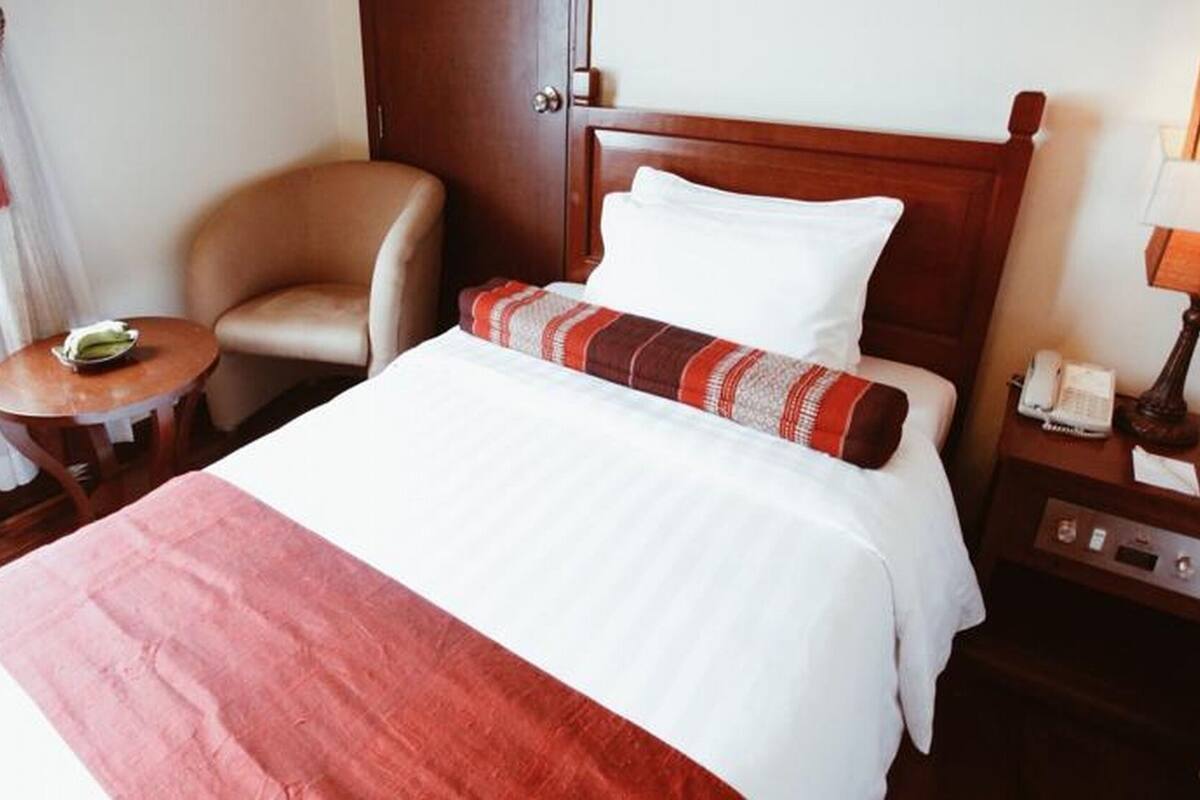 Hotellihuone, jossa on sänky, tuoli, pieni pöytä, yöpöytä ja ovi.