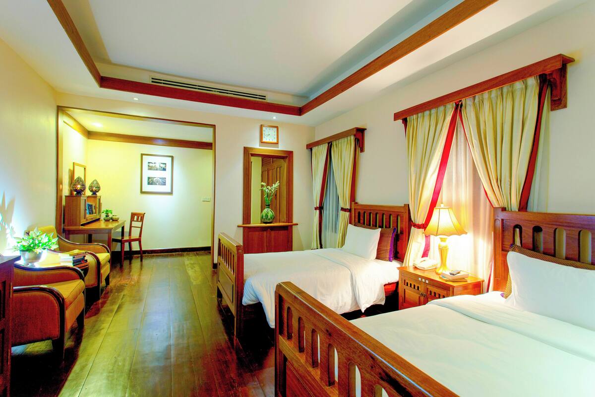 A hotel room with two beds, a desk, a chair, and a dining area.