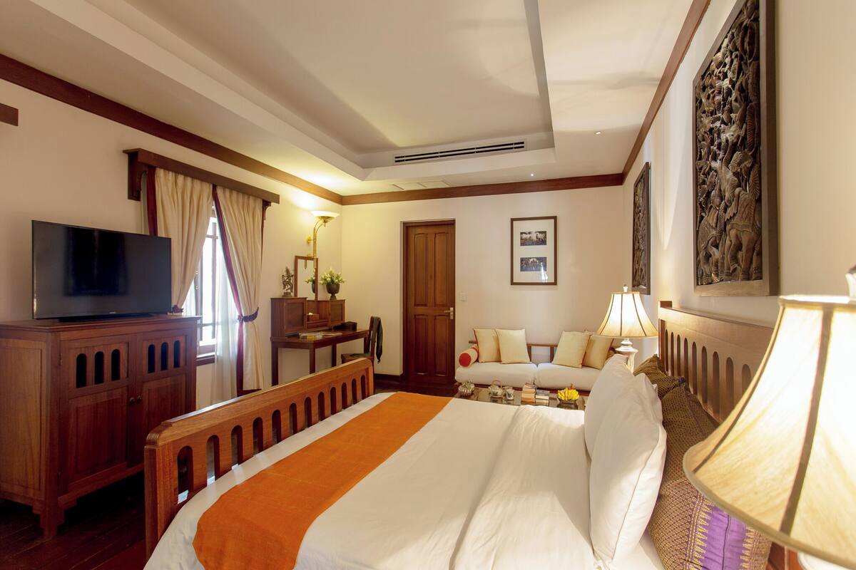 A hotel room with a bed, a desk with a TV, a sofa, a lamp, and artwork on the walls.