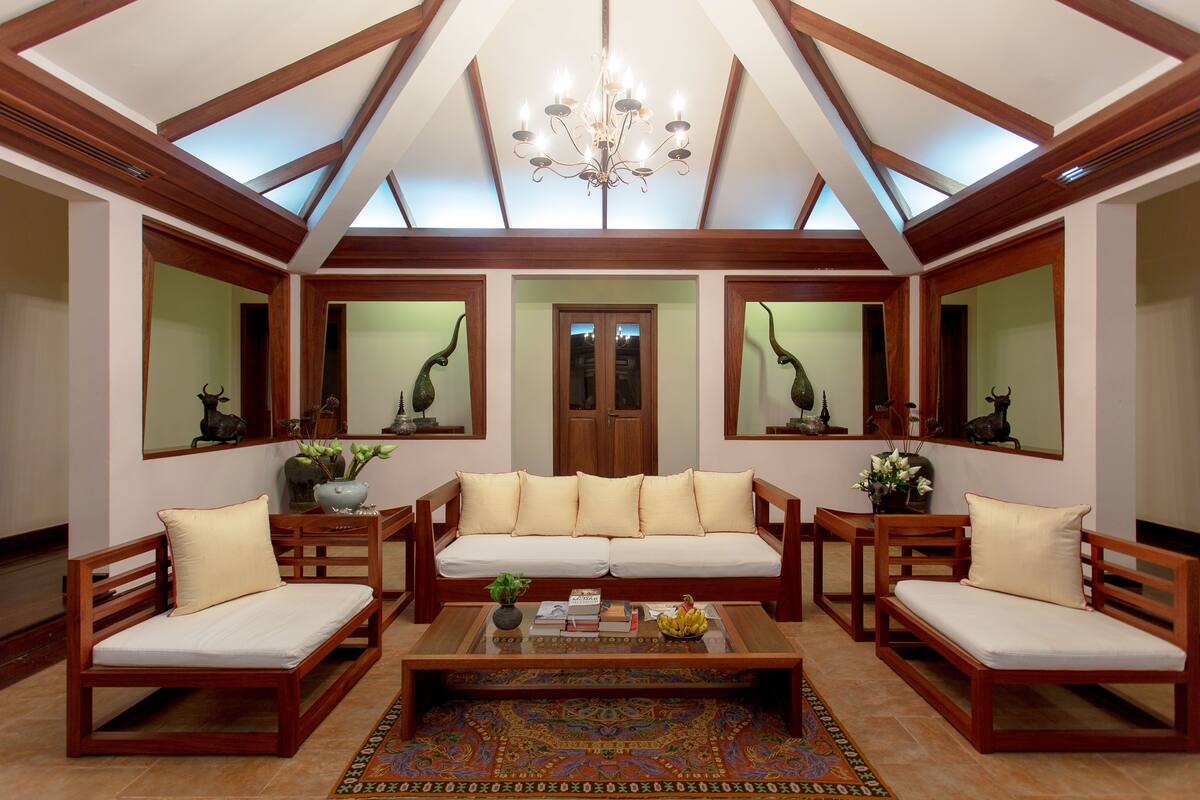 A spacious living area with a high ceiling, wooden furniture, and a central sofa.