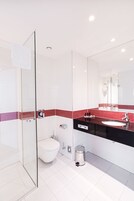 Uma casa de banho moderna com cabine de duche em vidro, sanita branca e lavatório preto com painel de azulejos vermelhos.