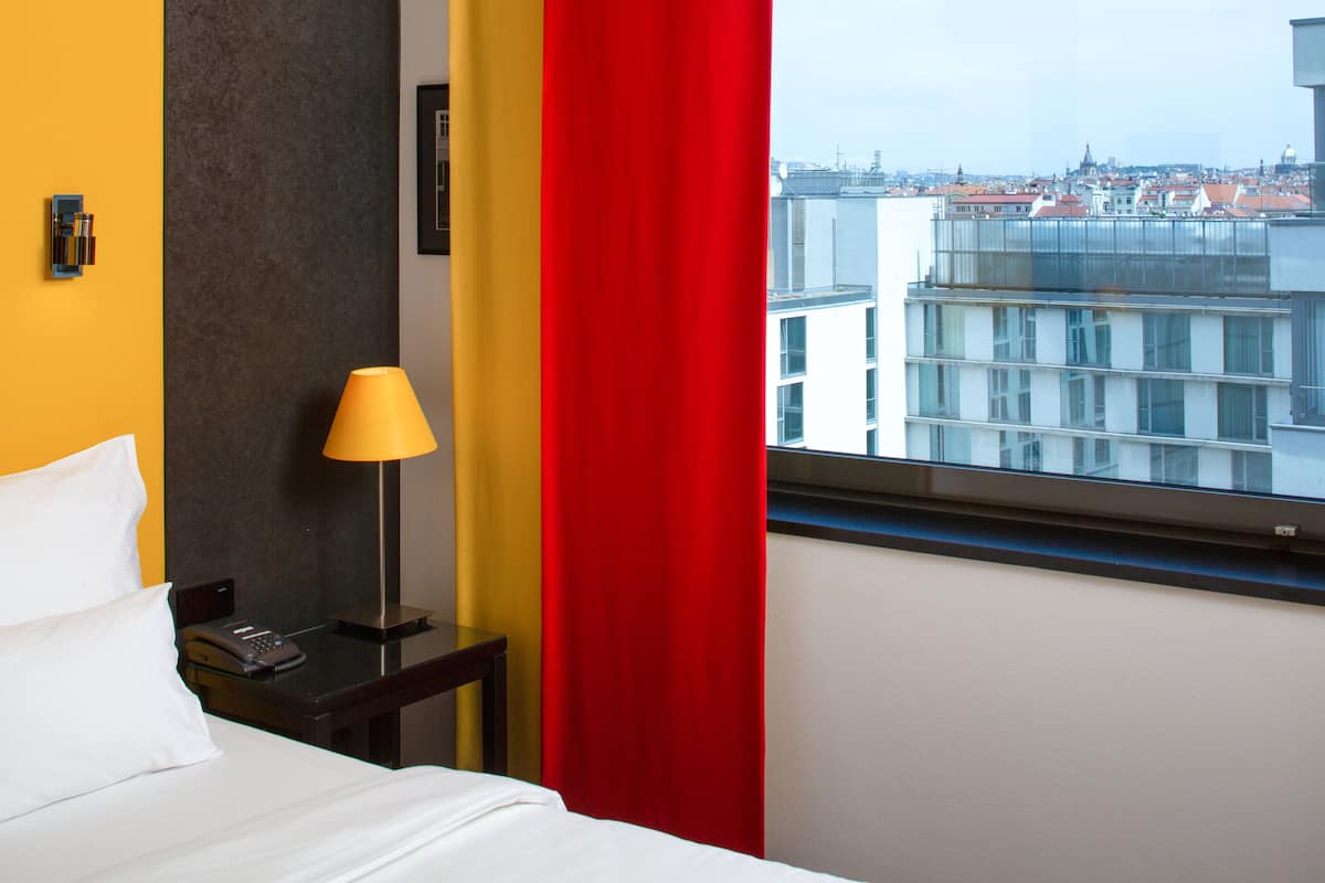 Une chambre d’hôtel avec un lit, une table de chevet avec une lampe et une fenêtre donnant sur la ville.