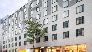 Un edificio moderno con fachada de ventanales rectangulares y un árbol en primer plano.