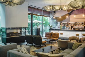 A modern lounge area with leather sofas, a fireplace, and a bar with various bottles. - OREA Hotel Angelo Praha (Prague)