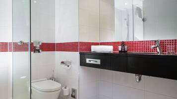 Un baño moderno con cabina de ducha de vidrio, inodoro blanco, tocador negro con espejo y salpicadero de azulejos rojos.