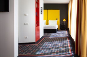 Quarto de hotel com cama, guarda-roupa vermelho, parede amarela e carpete estampado.