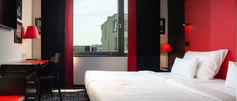 A hotel room with a bed, desk, chair, and a window with a view of buildings.