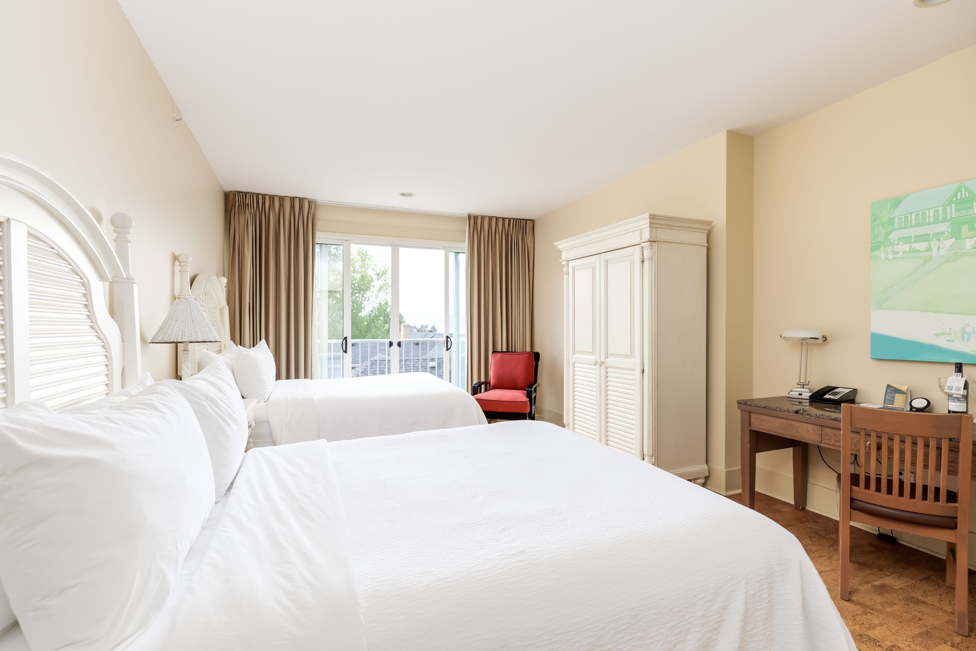 A hotel room with two beds, a desk, a chair, a wardrobe, and a window with curtains.