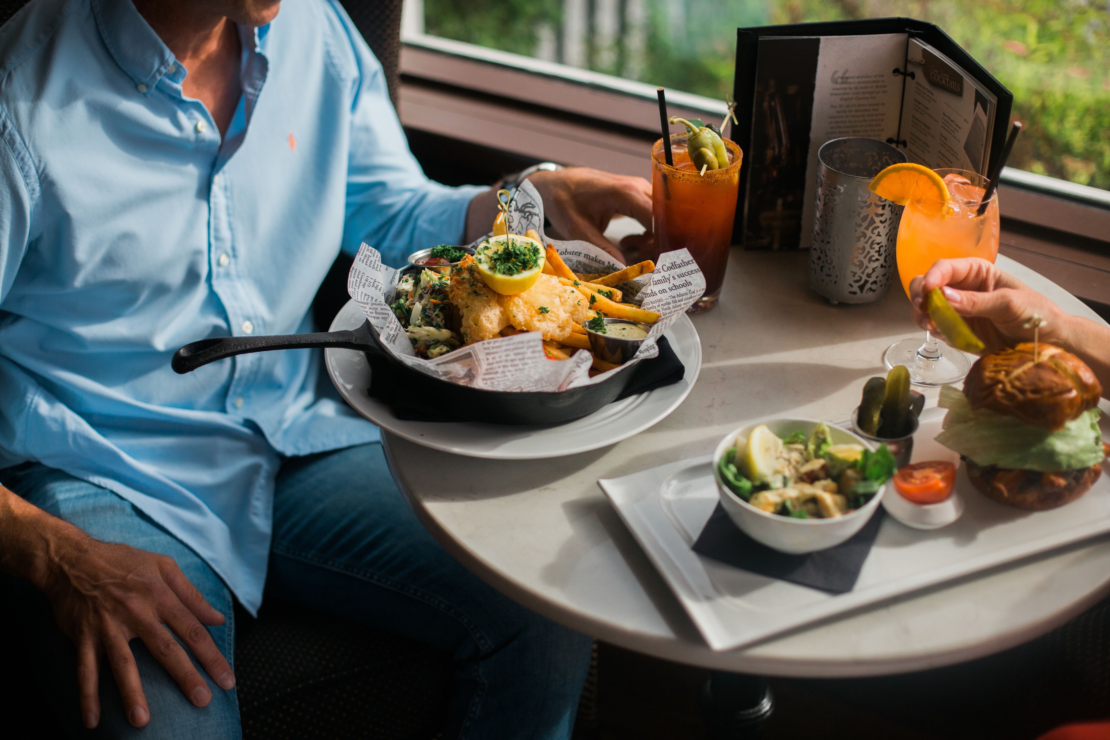 A dining table with a meal consisting of a burger, fries, and a salad, along with a Bloody Mary drink.