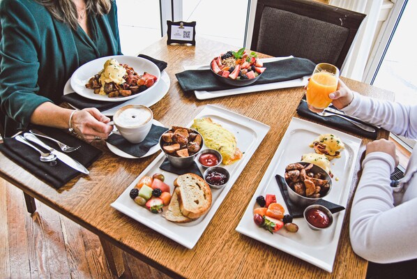 Una mesa de madera con diversos platos de desayuno, como huevos, fruta y pan.