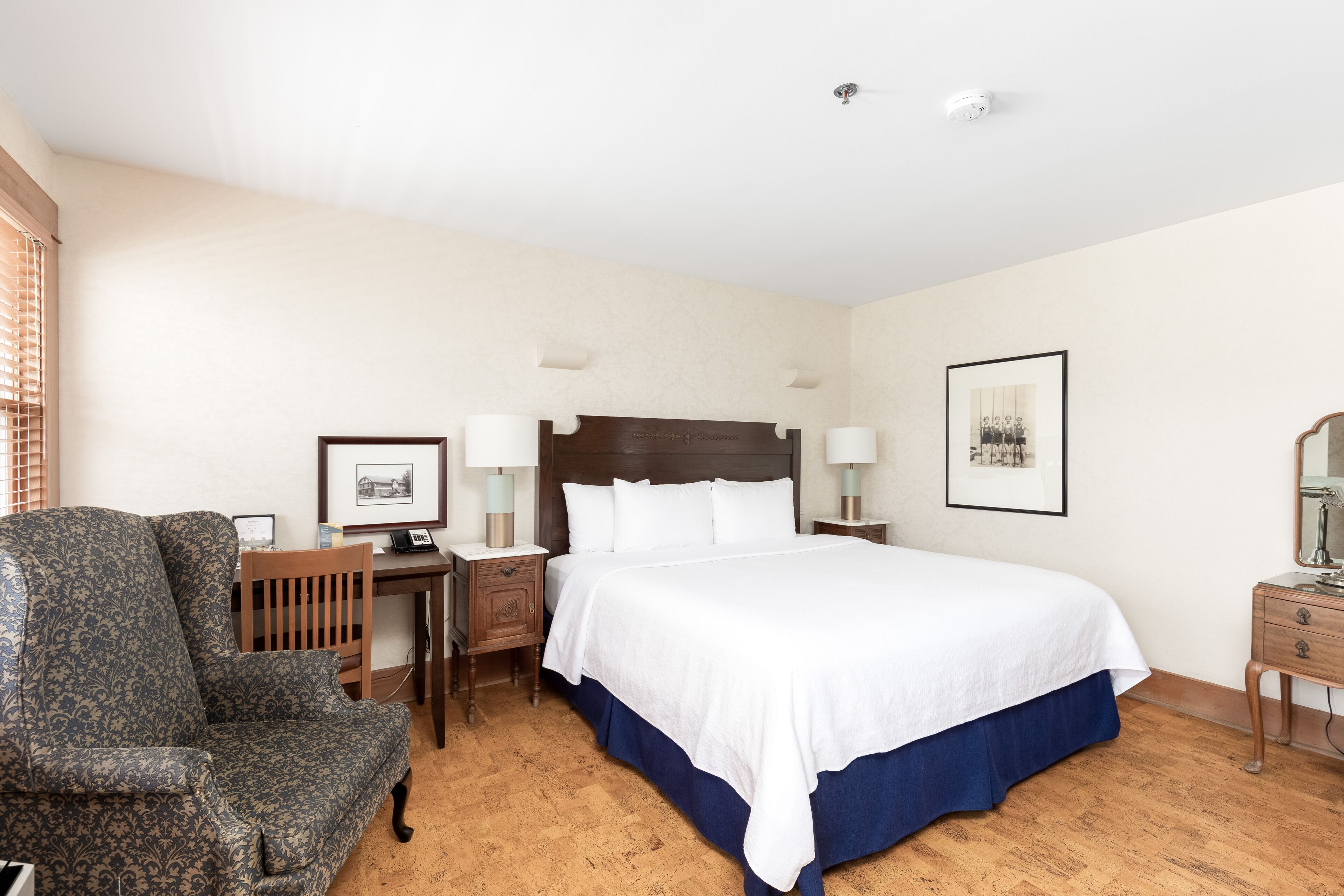 A hotel room with a large bed, a wooden chair, a desk, and a nightstand.