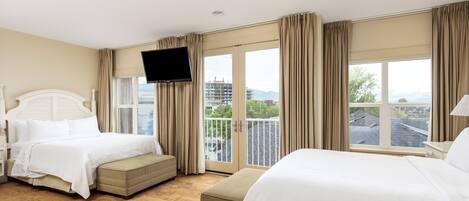 A hotel room with two beds, a flat-screen TV, and a balcony with a city view.