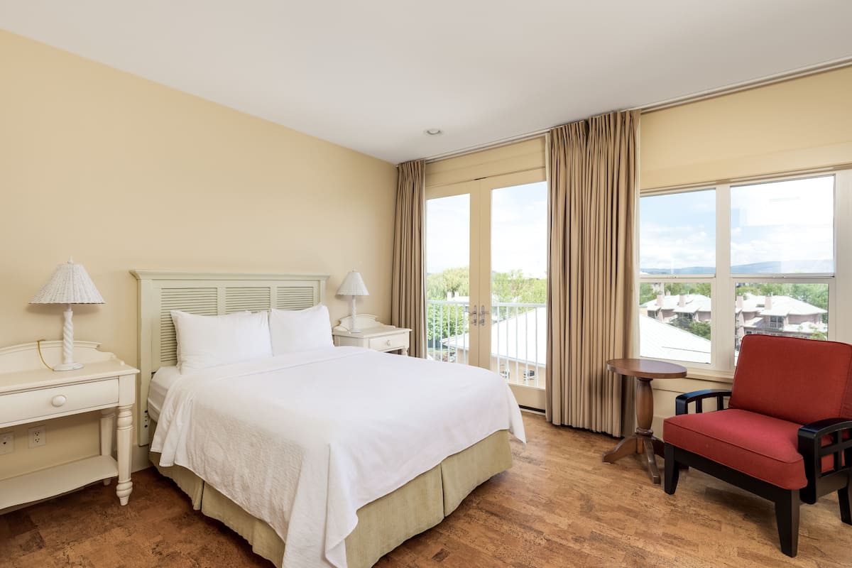 Ein Hotelzimmer mit einem Bett, Nachttischen, einem Sessel und einem Balkon mit Blick.
