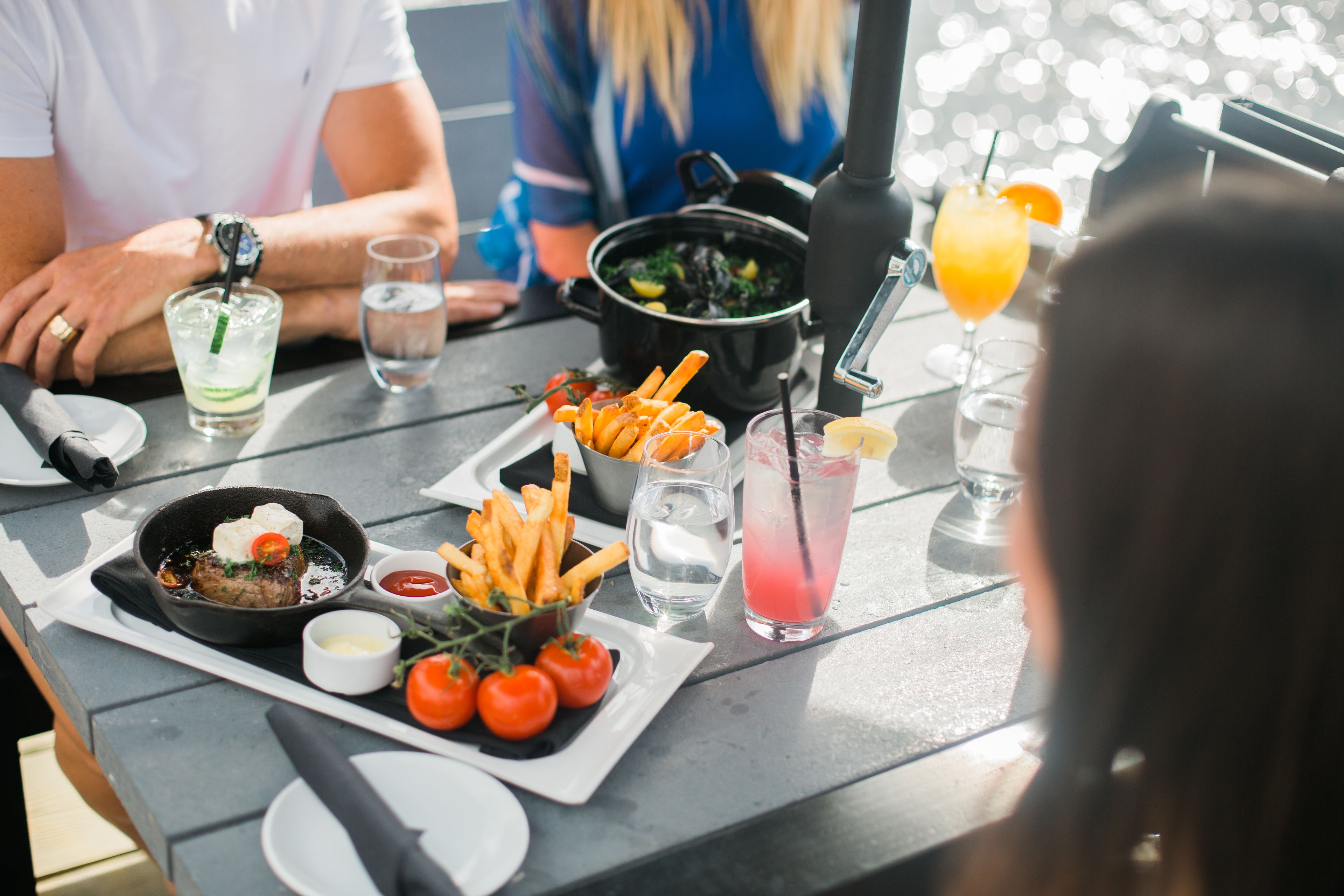 Une table à manger sur laquelle on trouve une variété de plats, notamment une poêle contenant de la viande, des frites et des tomates, ainsi que des boissons et un pot de soupe.