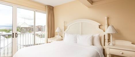 A hotel room with a large bed, two bedside tables, a window with a view of buildings, and a balcony.