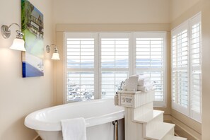 A bathroom with a bathtub, a window with blinds, a towel rack, and a wall-mounted air conditioning unit.