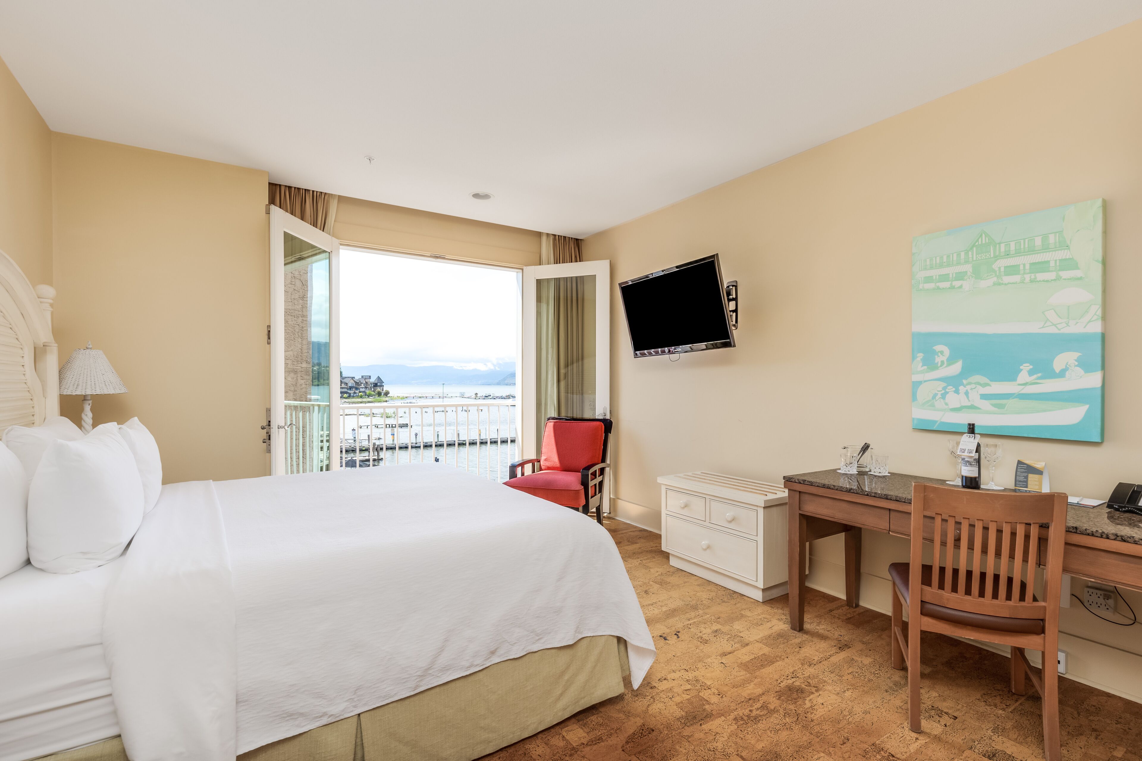 A hotel room with a large bed, a desk, a chair, a TV, and a balcony with a view.