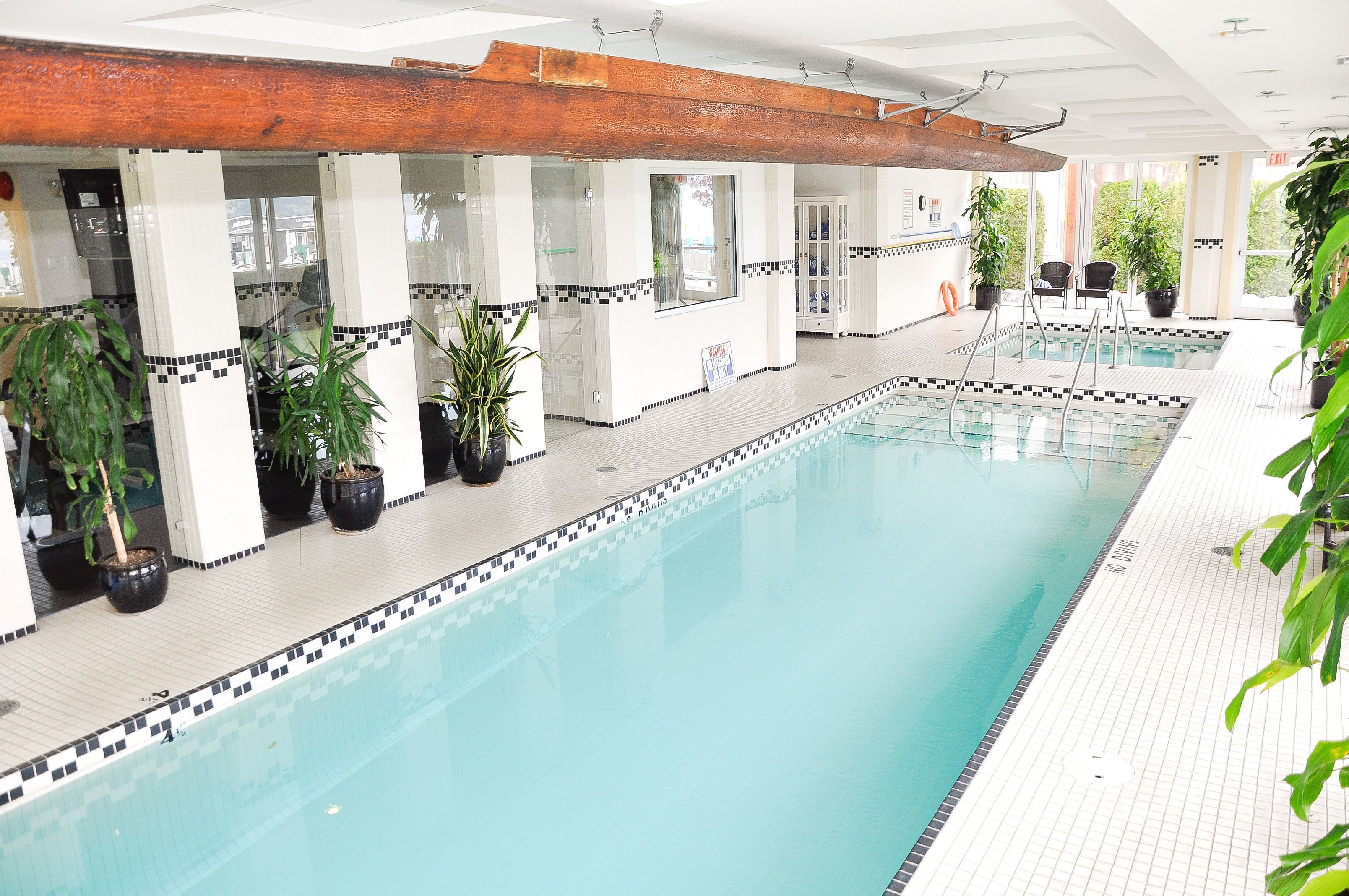 An indoor swimming pool with tiled walls, potted plants, and a wooden ceiling beam.