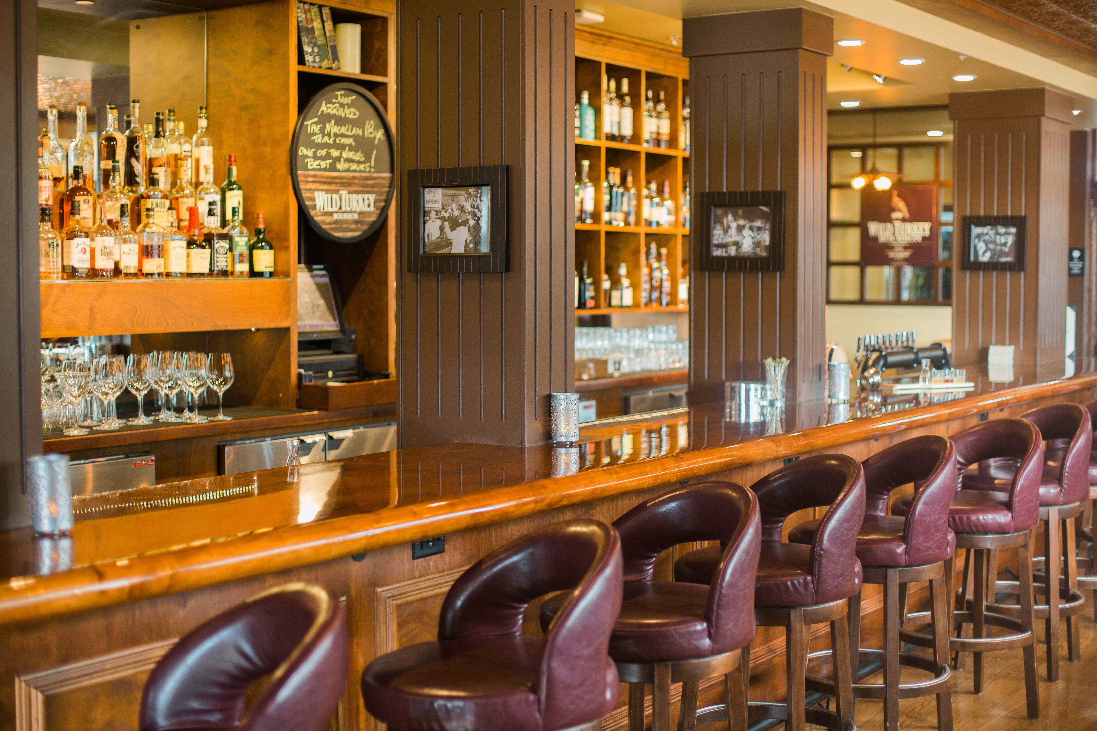 A bar area with multiple liquor bottles, glasses, and a wooden bar counter.